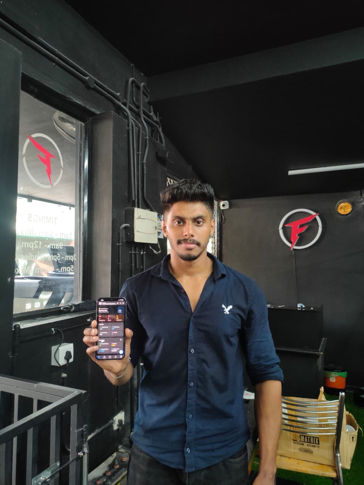 Hafis at Forge Fitness, holding his phone with the REPZ app open beside the gym's logo on the wall.