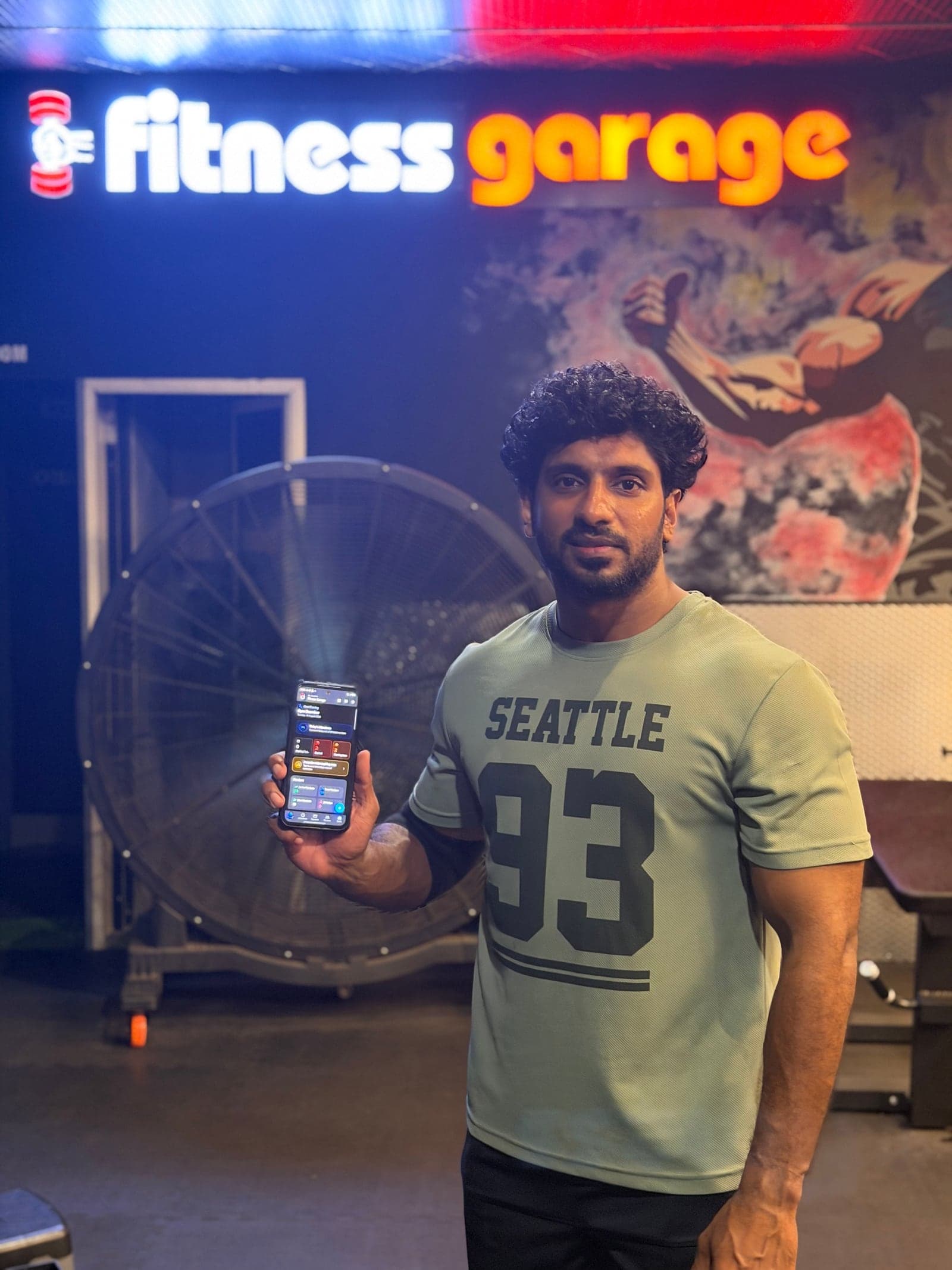 Hashim on the floor at Fitness Garage BKV, holding his phone with the REPZ owner dashboard open.