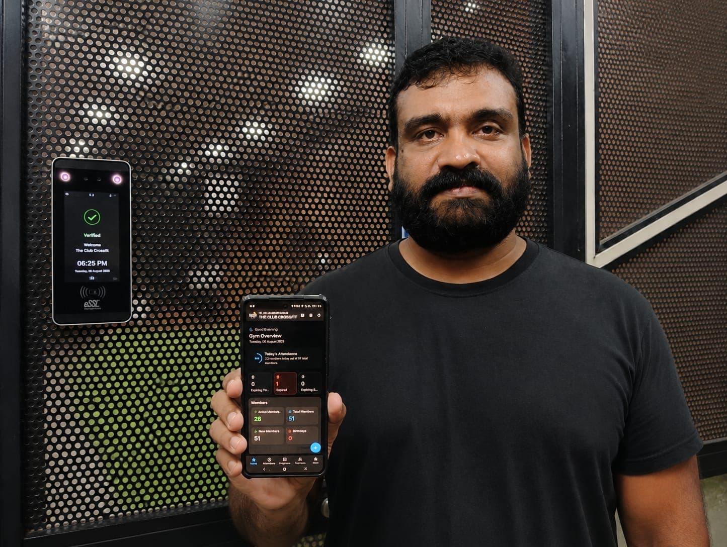 Riju Rajendran at The Club Crossfit, holding the REPZ app beside the biometric device on the gym door as it verifies a member.